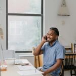 Adult man engaged in office work, speaking on phone, showcasing a professional environment.