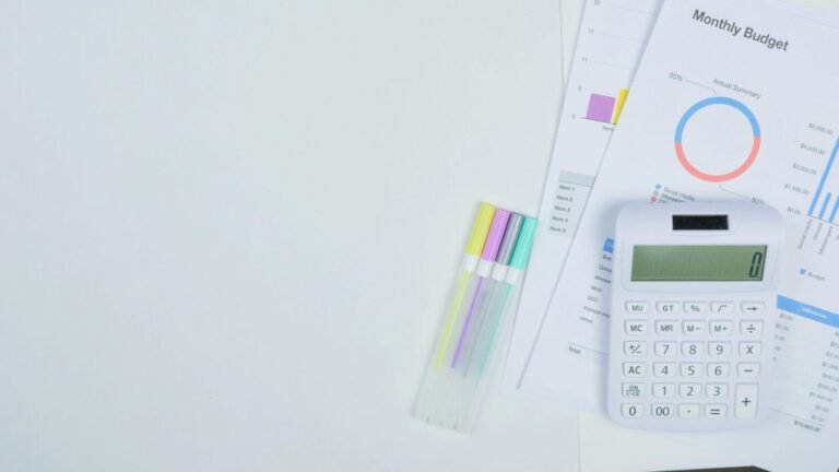 Minimalist office desk with a calculator, budget planning documents, and colorful pens.